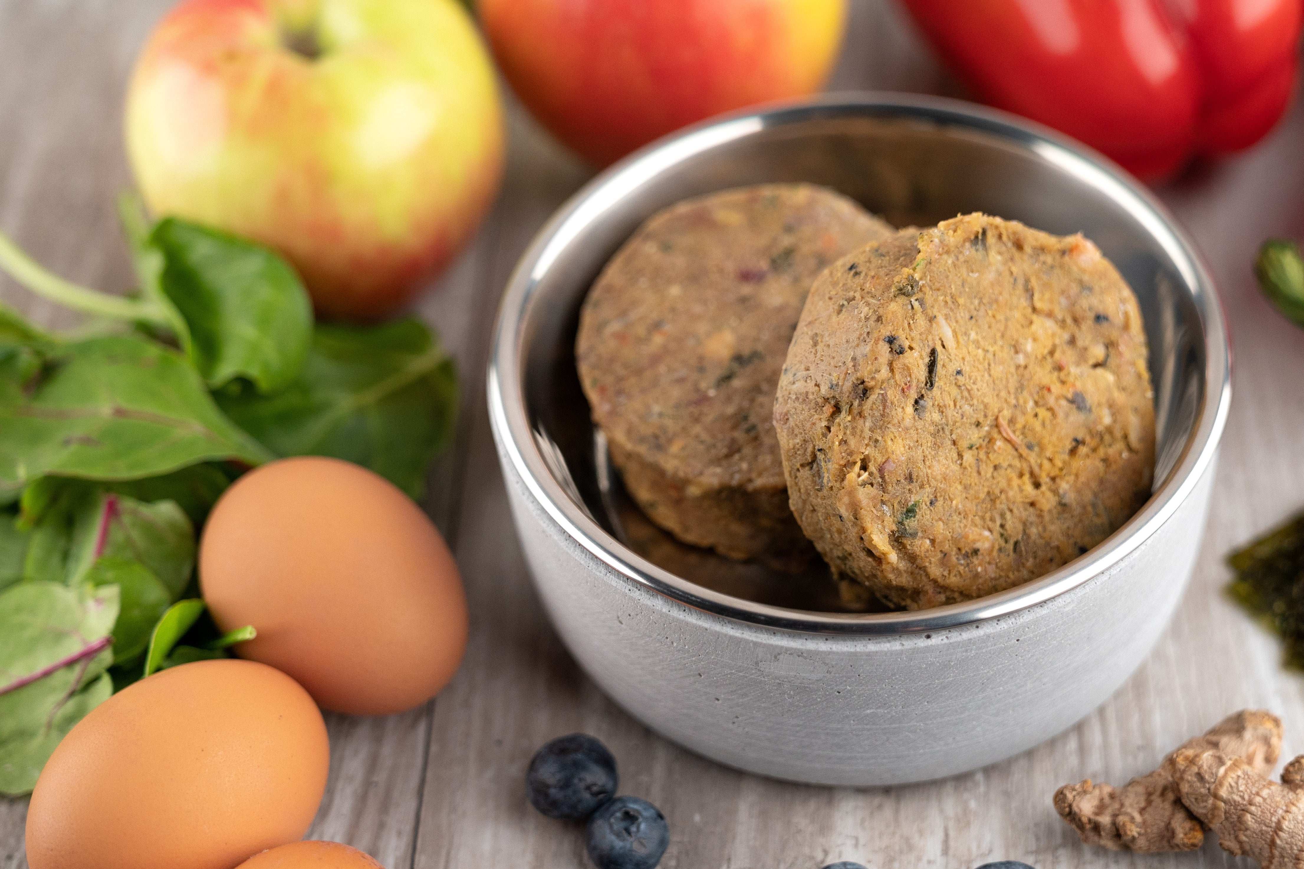 Bowl of pet food with fruits, vegetables, and eggs on a wooden surface